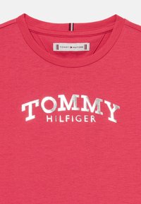 Tricou roșu din bumbac, cu guler rotund, având logo-ul argintiu "TOMMY HILFIGER" pe piept și ornament contrastant la guler.