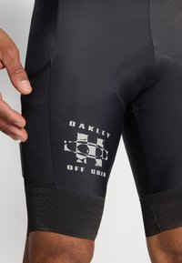 Fekete sportshorts textúrált derékpánttal és "Oakley Off Grid" felirattal. Simára kidolgozott anyag és testhezálló fazon jellemzi.