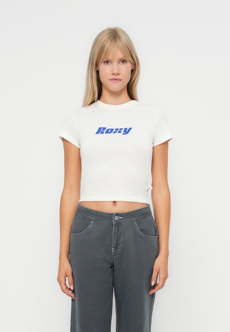 White cropped t-shirt with blue "Roxy" logo, short sleeves, and a minimalist design, paired with gray high-waisted pants.