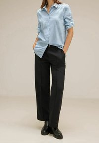 Ljusblå, långärmad skjorta med vita vertikala ränder; kombinerad med svarta vida byxor och svarta ankelstövlar.