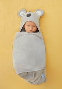 Manta de bebé gris con temática de animal, con capucha que presenta orejas, envuelta alrededor de un bebé. Tejido suave y texturizado sobre un fondo amarillo.