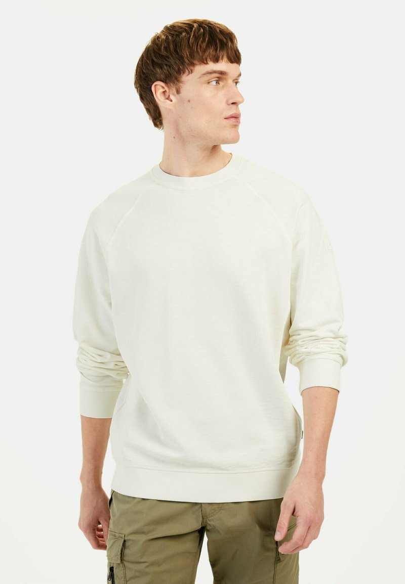 Helle beige Sweatshirt mit Raglanärmeln, Rundhalsausschnitt und gerippten Bündchen. Weiche Textur, minimalistisches Design, kombiniert mit olivfarbenen Cargo-Hosen.