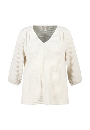 Blouse à manches longues texturée crème avec col en V et plis subtils aux épaules, présentée sur fond blanc.