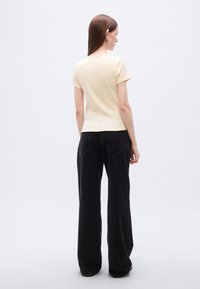 Κίτρινη εφαρμοστή κοντομάνικη μπλούζα, συνδυασμένη με ψηλόμεσα μαύρα τζιν με φαρδύ πόδι. Λεία υφή, απλός σχεδιασμός, ελάχιστες λεπτομέρειες.