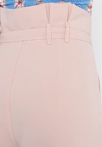 Ljusrosa byxor med hög midja och slät textur. Har bältesöglor och en snygg veckdetalj vid midjan som ger ett strukturerat utseende.