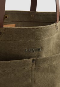 Sac cabas en toile vert olive muni de poignées en cuir marron, de coutures décoratives, d'une poche avant et d'un logo "Levi's" embossé sur le côté.