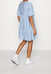 Ljusblommig klänning med korta ärmar, flätad kjol och nyckelhålsdetalj i ryggen, tillsammans med vita kanvas högklackade sneakers.