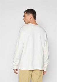 White long-sleeve shirt with a round neckline and straight hem, paired with light tan pants, showing a smooth texture and casual design.