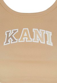 Beige sports-bh med ribbet tekstur. Har dristig "KANI"-bokstaver i krem og lysebrun, rund halslinning, og tettsittende design.