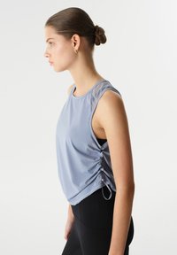 Lichtblauw sportief tanktop met een mesh schouder, geplooide zijkanten en een ontspannen pasvorm. Draagt met zwarte legging; gladde stof en casual ontwerp.