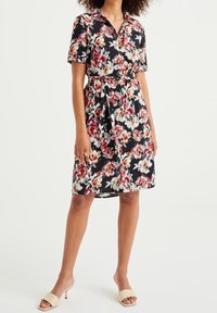 Robe noire à manches courtes avec un motif floral en rouge, blanc et jaune ; taille cintrée avec un nœud, longueur genou, fabriquée en tissu léger.