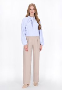 Lyseblå bluse med knyttet halsudskæring, lange ærmer, parret med beige højtaljede plisserede bukser. Glat stof, elegant silhuet.