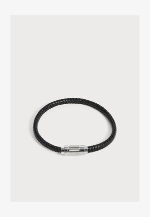 Schwarzes geflochtenes Lederarmband mit einem zylindrischen silbernen Magnetverschluss auf einem schlichten, hellen Hintergrund.