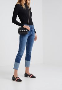 Black ribbed long-sleeve top, blue cuffed skinny jeans, black loafers with red and gold accents, and a black handbag with pearl details.