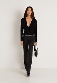 Czarna bluzka z długim rękawem i drapowanym dekoltem, zestawiona z czarnymi spodniami. Dodatki obejmują elegancką srebrną torebkę i pasek ozdobiony kryształkami.