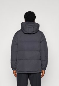 Grey padded jacket with a hood, featuring a quilted design, long sleeves, and elastic cuffs. The texture appears smooth and insulated.