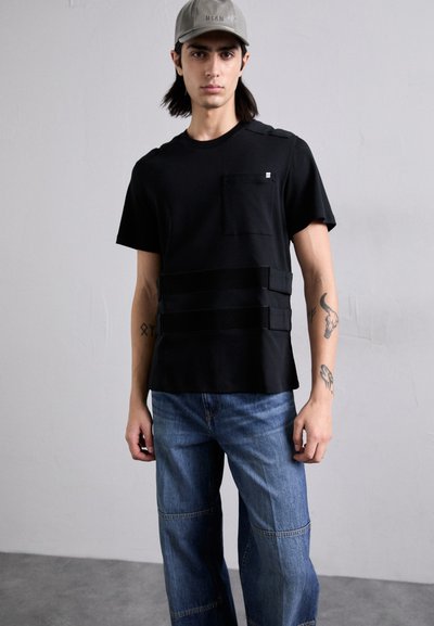 Fekete, rövid ujjú póló, elöl zsebből készült, három vízszintes pánttal díszítve. Világoskék, laza szabású farmernadrággal párosítva.