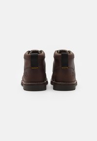 Bottines en cuir marron avec un col rembourré, une languette élastique et des coutures contrastantes. Semelle robuste avec des détails de logo sur le talon.