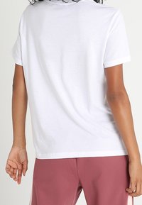 Vit t-shirt med kort ärm och rundad halsringning, med subtil textur, som är ihop med rosa träningsbyxor. Synliga sömdetaljer på baksidan.