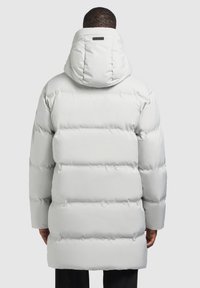 Fehér pufi dzseki kapucnival, vízszintesen varrott panelek jellemzik, sima külső felülete van, és minimális logó részlet található a hátsó részén.