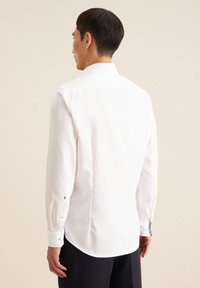 Weißes Langarmhemd mit spitzem Kragen und Knopfmanschetten. Glatter Stoff, leicht abgerundeter Saum und minimalistisches Design.