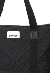 Kviltad svart tote-väska med ett texturerat mönster och hållbara remmar. Har en vit etikett med "DAY ET" i fet stil.