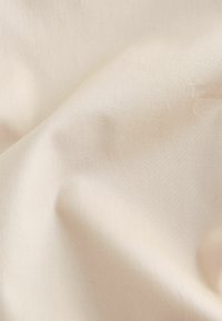 Tissu lisse de couleur crème avec des plis subtils et une texture fine, montrant des reflets de lumière à sa surface.