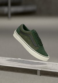 Green suede sneaker with a white rubber sole and dark green accents. Features rounded toe, flat laces, and side stripe detail.