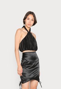 Top halter preto com textura plissada e pescoço amarrado. Saia mini de cetim com franzidos laterais e detalhes de cordão. Design suave e ajustado ao corpo.