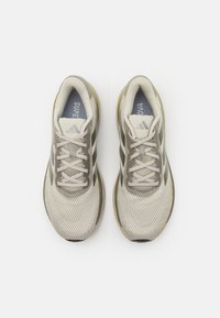 Beige Sport-Schuhe mit Mesh-Obermaterial, leichter Polsterung, verstärkter Zehenkappe und grauen Akzenten. Dicke Gummisohle mit strukturiertem Muster.