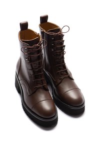 Ein Paar dunkelbraune Leder-Schnürstiefeletten mit schwarzen, dicken Sohlen und seitlichen Reißverschlüssen auf einem weißen Hintergrund.