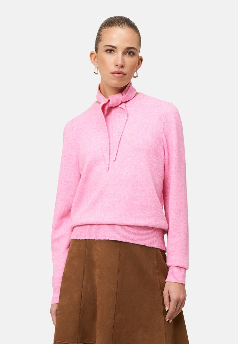 Pink cashmere sweater with a ribbed hem and a knotted collar detail, paired with a brown suede skirt, against a white background.