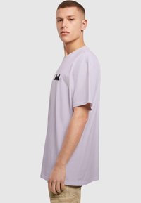 Lavender cotton t-shirt featuring a black cat graphic on the front, relaxed fit, short sleeves, and a round neckline.