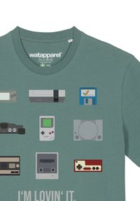 Teal T-shirt met retro gameconsole graphics in verschillende kleuren. Heeft een ronde hals en de tekst "I'M LOVIN' IT" in het wit onderaan.