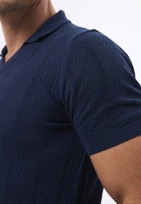 Navyblaues gestricktes Poloshirt mit strukturiertem Muster, kurzen Ärmeln und klassischem Kragen. Das Material ist leicht und hat ein atmungsaktives Design.