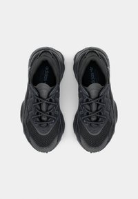 Zapatillas deportivas negras con un upper de malla texturizada, cordones resistentes y una suela acolchada. El diseño es aerodinámico con acentos sutiles.