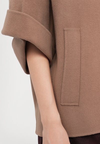 Top en polaire marron avec des manches retroussées et une poche latérale, présentant une texture douce et une silhouette décontractée.