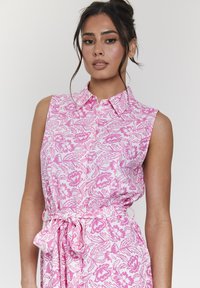 Abito senza maniche in bianco con motivo floreale rosa, caratterizzato da un colletto e una cintura in vita. Tessuto leggero e texture.