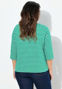 Grün-weiß gestreiftes Langarmoberteil mit Rundhalsausschnitt und Dreiviertelärmeln, kombiniert mit dunklen Jeans. Glatte Stofftextur.