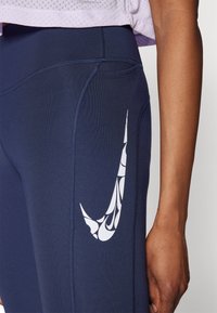 Marineblauwe sportlegging met een wit Nike-logo, voorzien van een spiraalpatroon op de bovenbeen. De stof is rekbaar en heeft zichtbare stiksel-details.