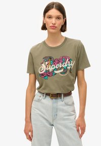 Olijfgroene katoenen t-shirt met een kleurrijke geborduurde afbeelding van bloemen en een slang, met de tekst "Superdry" in een cursieve lettertype.