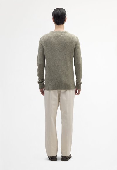 Maglione verde oliva in maglia a trama, con colletto a girocollo e polsini a costine, abbinato a pantaloni a gamba larga color crema.