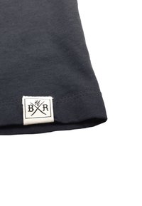 T-paita tummansinisestä puuvillasta, jossa on teksturoitu pinta. Helma on varustettu valkoisella tarralla, jossa on musta teksti ja ristikkäiset välineet.