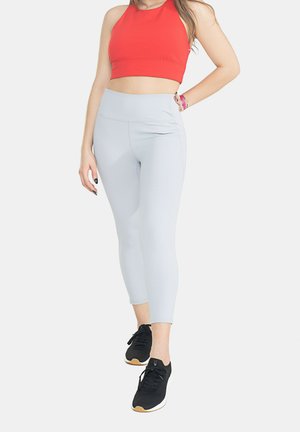 Leggings grigi chiari con una texture liscia e una vita alta, abbinati a un crop top rosso e scarpe da ginnastica nere.