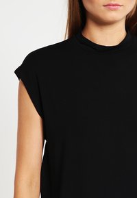 Top sans manches noir avec un col montant, en coton doux, texture lisse et coupe décontractée. Aucune motif ou matériel visible.