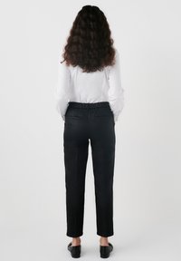 Zwarte op maat gemaakte broek met een platte tailleband en twee achterzakken, gecombineerd met een witte blouse met lange mouwen. Glad materiaal, enkel lengte.