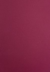 Priliehavá tkanina v hlbokej burgundskej farbe s hladkou textúrou a jemným ryhovaným vzorom, ktorý zdôrazňuje jej pružnosť a priliehavý dizajn.