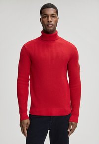 Rode, gebreide coltrui met een gestructureerd patroon, geribbelde manchetten en zoom. Heeft een klein logoplaatje op de linkermouw.