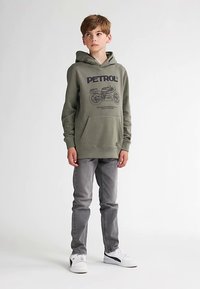 Grön huvtröja med motorcykelgrafik och texten "PETROL", tillsammans med grå jeans och vita sneakers, i en avslappnad outfit.