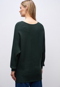 Dunkelgrüner gerippter Pullover mit weitem Ausschnitt und langen Ärmeln, der eine lockere Passform und seitliche Schlitze für mehr Bewegungsfreiheit bietet.